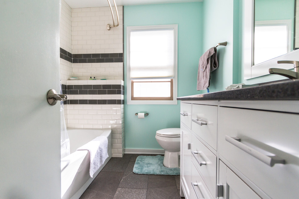 Cette image montre une salle de bain marine de taille moyenne avec un placard à porte shaker, des portes de placard blanches, une baignoire en alcôve, un carrelage noir et blanc, un carrelage métro, un mur bleu, un sol en ardoise, un lavabo encastré, un sol noir et une cabine de douche avec un rideau.