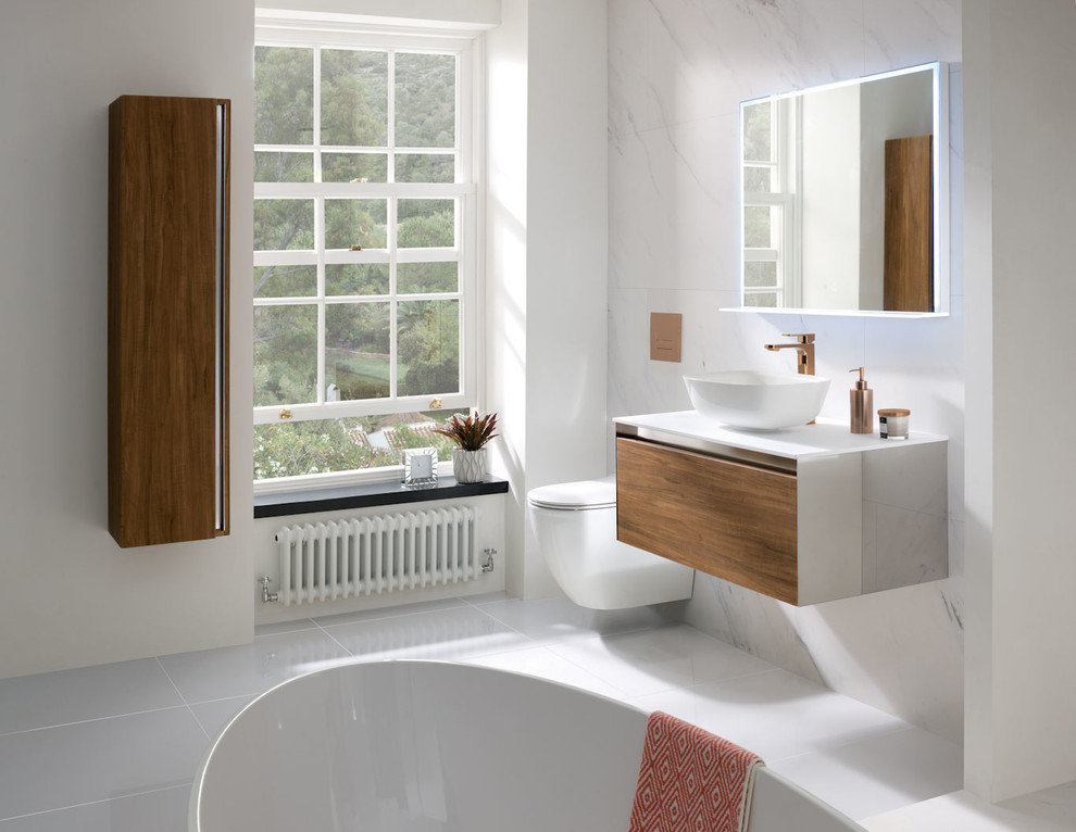 Mediterranean family bathroom in West Midlands with flat-panel cabinets, medium wood cabinets, a freestanding bath, a wall mounted toilet, porcelain flooring, a vessel sink, solid surface worktops, grey floors and white worktops.