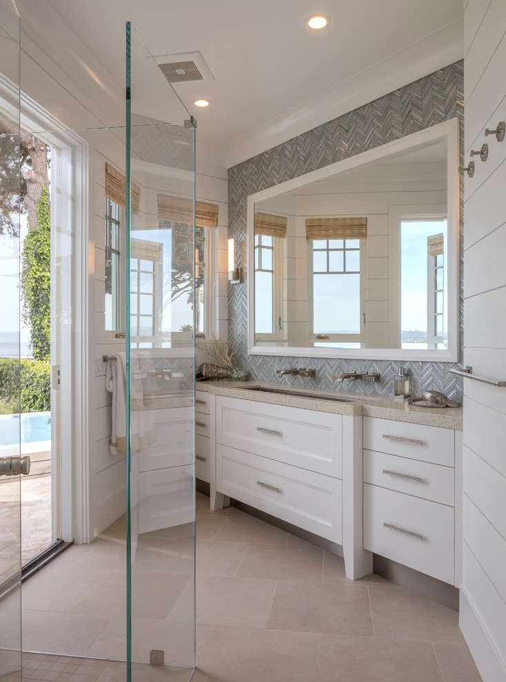 This is an example of a beach style bathroom in Sacramento with recessed-panel cabinets, white cabinets, a corner shower, grey tiles, mosaic tiles, white walls, a trough sink, beige floors, a hinged door and beige worktops.