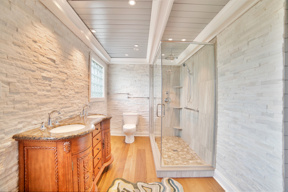 Cette photo montre une salle de bain chic en bois brun avec un placard en trompe-l'oeil, une douche d'angle, un carrelage blanc, des dalles de pierre, un mur blanc, un sol en carrelage imitation parquet, un plan de toilette en granite, un sol marron, une cabine de douche à porte battante, un plan de toilette multicolore, meuble double vasque, meuble-lavabo suspendu et un plafond voûté.
