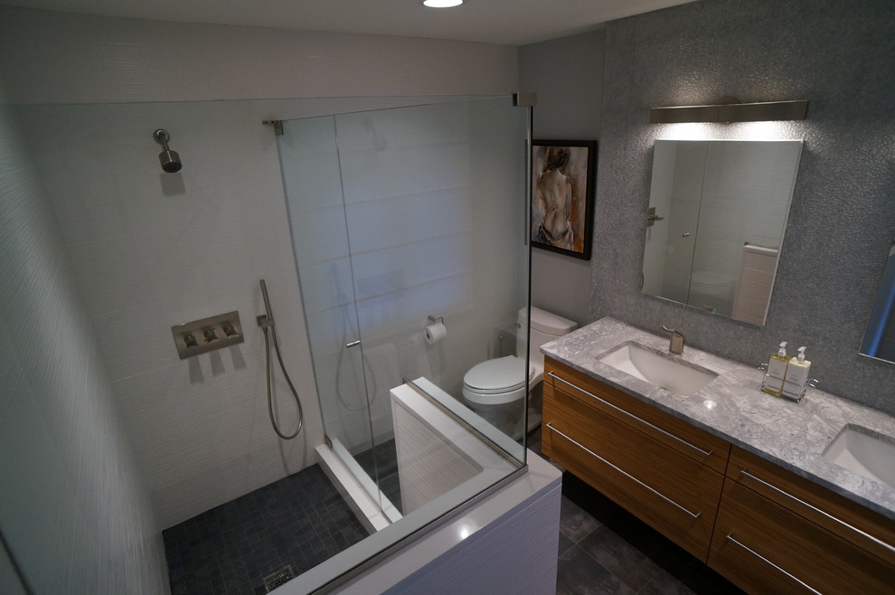 Inspiration for a medium sized modern ensuite bathroom in Philadelphia with a submerged sink, flat-panel cabinets, light wood cabinets, granite worktops, a corner shower, grey tiles, a two-piece toilet, grey walls, ceramic flooring, brown floors and a hinged door.