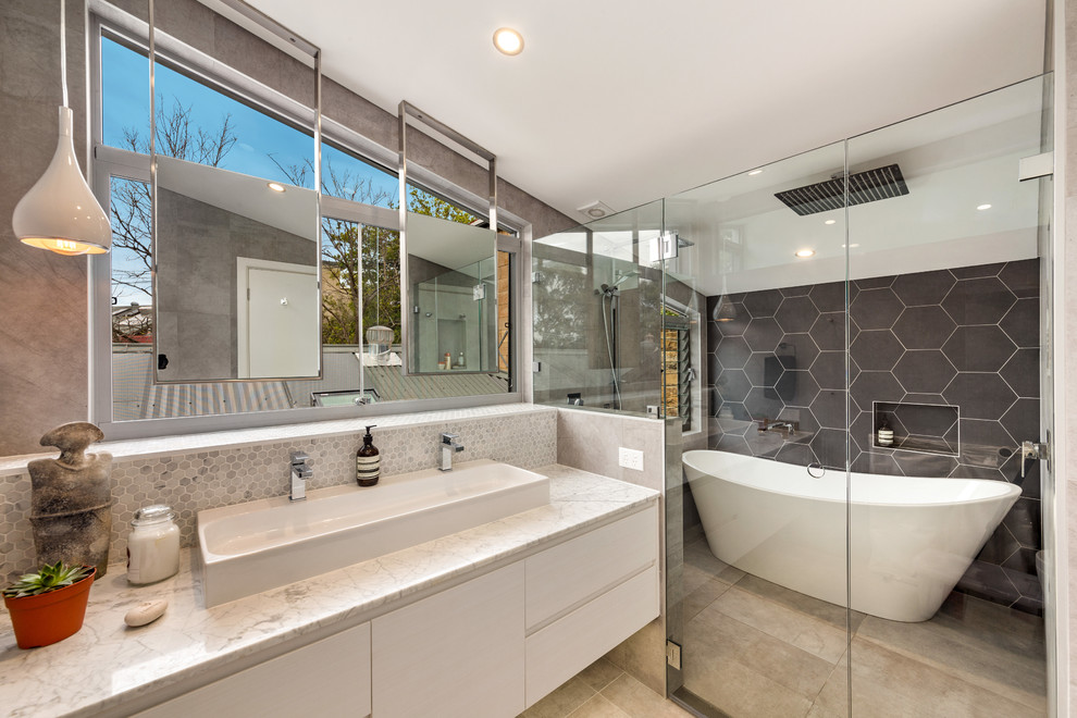 Idéer för ett mellanstort modernt en-suite badrum, med vita skåp, ett fristående badkar, grå kakel, porslinskakel, grå väggar, klinkergolv i keramik, marmorbänkskiva, släta luckor, en dusch/badkar-kombination och ett avlångt handfat