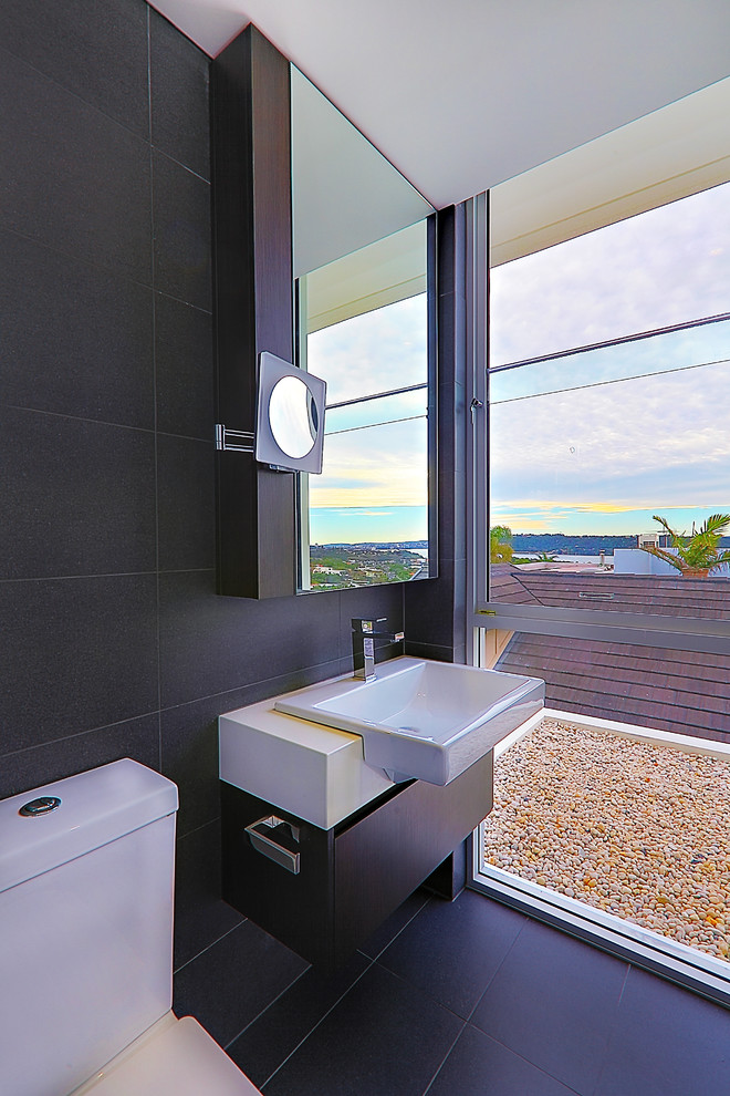 Réalisation d'une salle de bain design en bois foncé avec une grande vasque, un placard à porte plane, WC séparés et un carrelage noir.