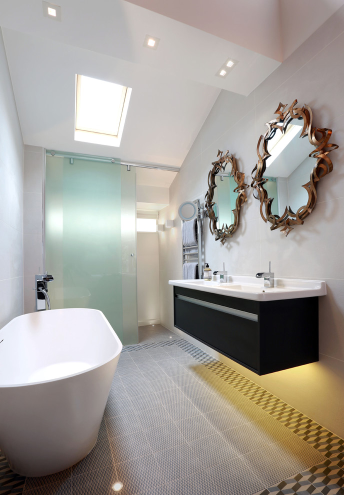 Стильный дизайн: главная ванная комната среднего размера в современном стиле с плоскими фасадами, синими фасадами, отдельно стоящей ванной, серой плиткой, керамогранитной плиткой, серыми стенами, полом из керамогранита и подвесной раковиной - последний тренд