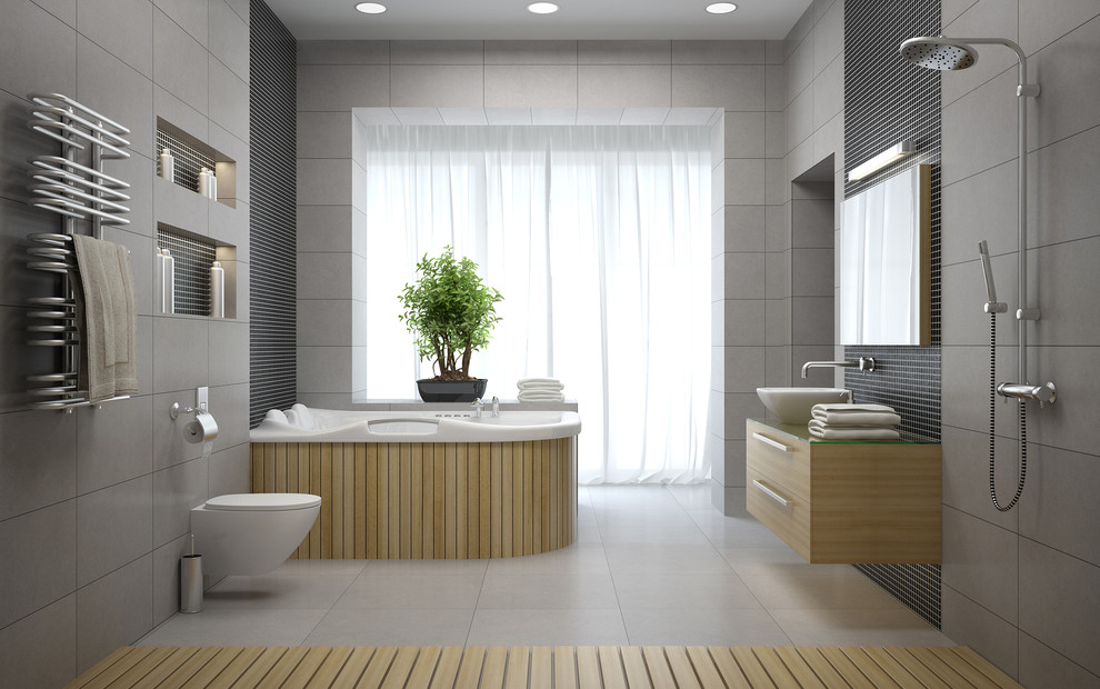 Foto på ett stort funkis en-suite badrum, med släta luckor, skåp i ljust trä, ett fristående handfat, bänkskiva i glas, ett platsbyggt badkar, en öppen dusch, grå kakel, keramikplattor, grå väggar, klinkergolv i keramik, grått golv, med dusch som är öppen och en vägghängd toalettstol