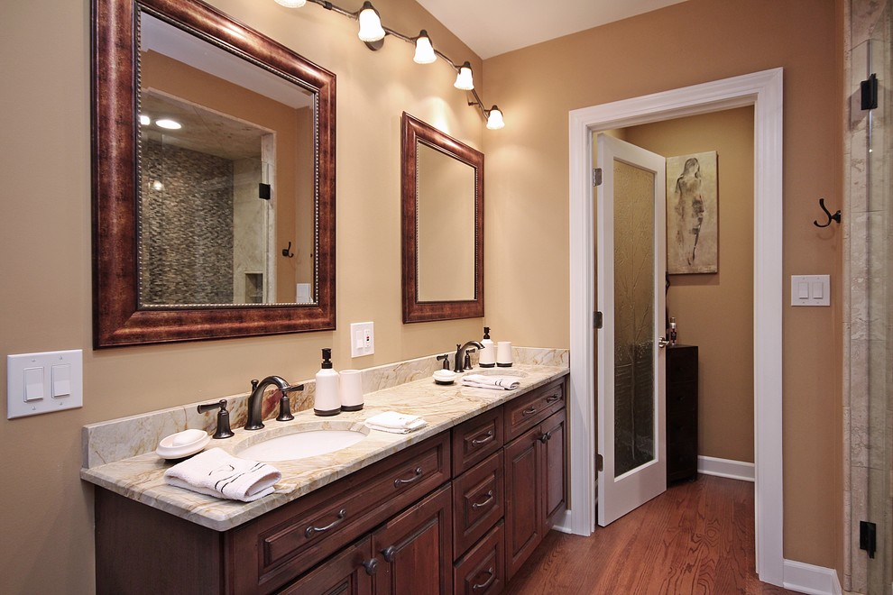 This is an example of a medium sized rustic ensuite bathroom in Chicago with a submerged sink, raised-panel cabinets, dark wood cabinets, limestone worktops, a corner bath, an alcove shower, a one-piece toilet, beige tiles, porcelain tiles, beige walls and medium hardwood flooring.