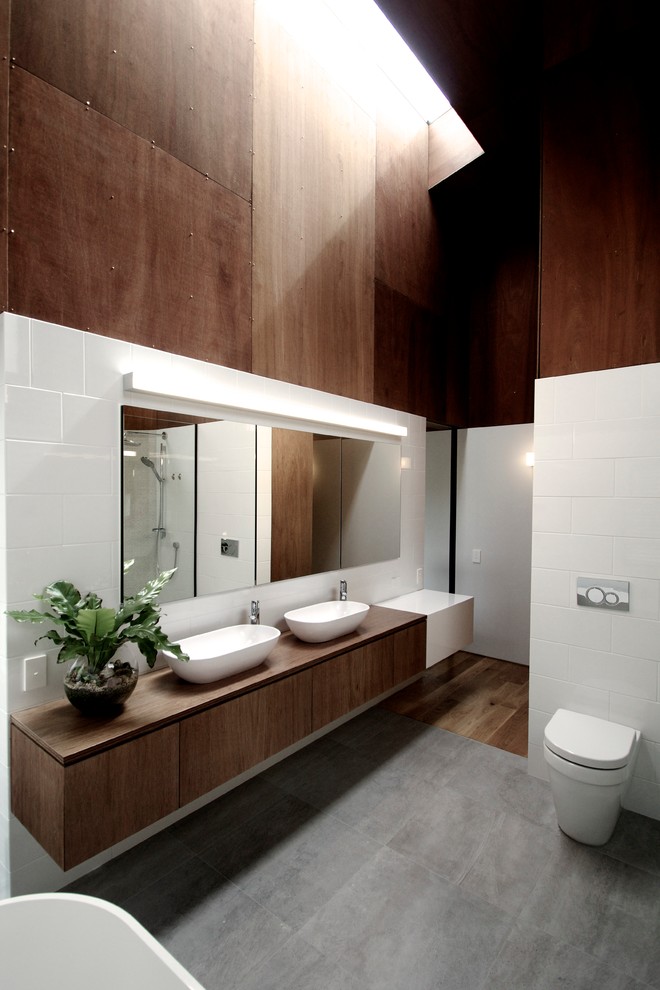 На фото: ванная комната среднего размера в современном стиле с плоскими фасадами, темными деревянными фасадами, отдельно стоящей ванной, унитазом-моноблоком, столешницей из дерева и коричневой столешницей