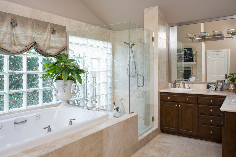 Medium sized classic ensuite bathroom in Orange County with raised-panel cabinets, dark wood cabinets, a built-in bath, a corner shower, a two-piece toilet, beige tiles, stone slabs, beige walls, travertine flooring, a built-in sink and marble worktops.