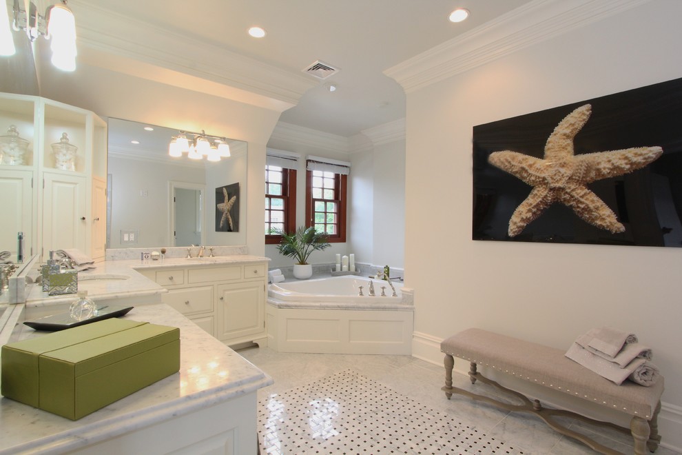На фото: большая главная ванная комната в стиле неоклассика (современная классика) с врезной раковиной, фасадами с выступающей филенкой, белыми фасадами, столешницей из гранита, угловой ванной, серой плиткой и серыми стенами с