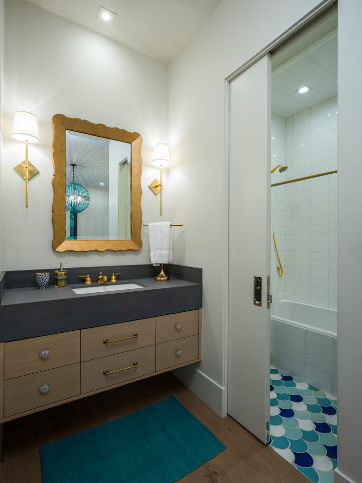 Cette image montre une salle de bain design en bois clair avec un placard à porte plane, une baignoire en alcôve, un combiné douche/baignoire, un carrelage blanc, un mur blanc, un sol en bois brun, un lavabo encastré, un sol marron et un plan de toilette gris.