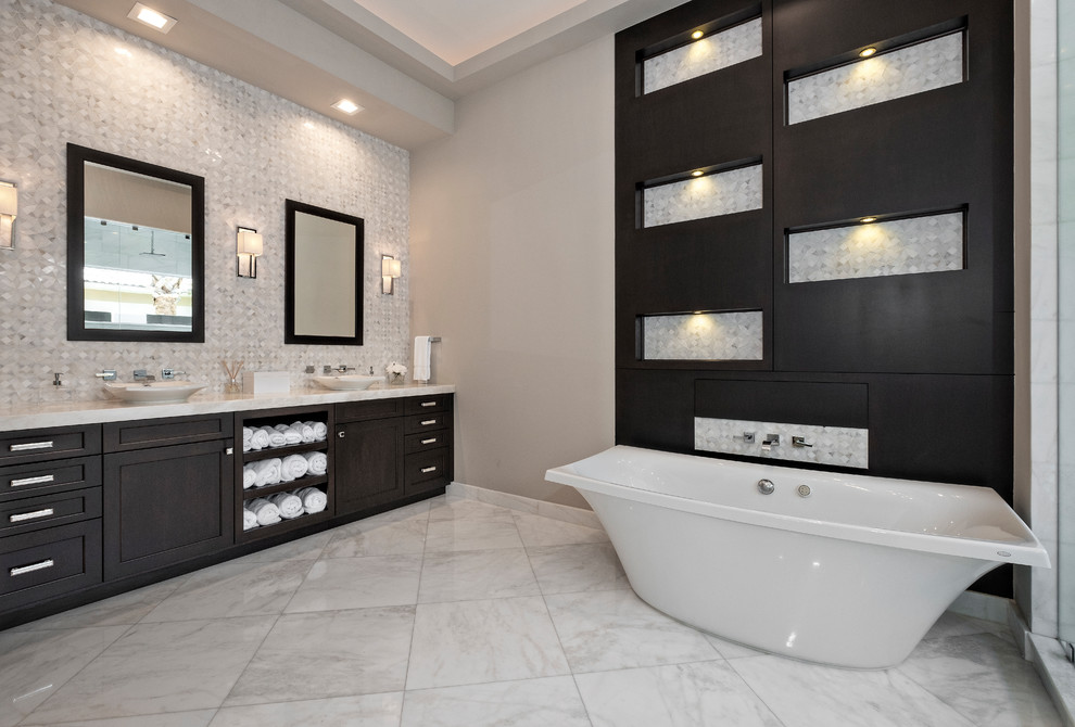 Modernes Badezimmer mit flächenbündigen Schrankfronten, freistehender Badewanne, beigen Fliesen, schwarzen Schränken, beiger Wandfarbe, Aufsatzwaschbecken, beigem Boden und beiger Waschtischplatte in Miami