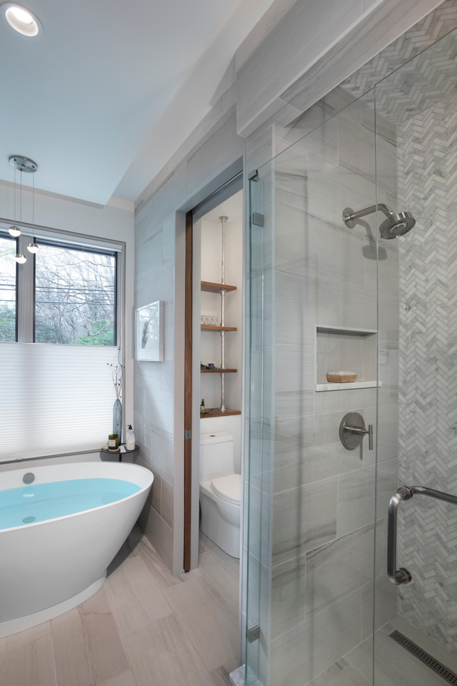 Cette photo montre une salle de bain principale tendance de taille moyenne avec une baignoire indépendante, une douche d'angle, WC à poser, un carrelage gris, du carrelage en marbre, un mur gris, parquet clair, un sol beige et une cabine de douche à porte battante.