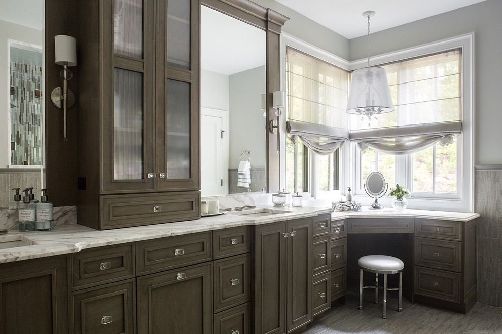 Klassisk inredning av ett mellanstort en-suite badrum, med skåp i shakerstil, bruna skåp, en dusch i en alkov, en toalettstol med hel cisternkåpa, grå kakel, porslinskakel, grå väggar, klinkergolv i porslin, ett nedsänkt handfat och marmorbänkskiva