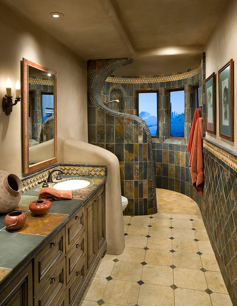 This is an example of an ensuite bathroom in Phoenix with a submerged sink, tiled worktops, a built-in shower, dark wood cabinets, brown tiles, grey tiles, recessed-panel cabinets, slate tiles, beige walls, travertine flooring, beige floors and an open shower.