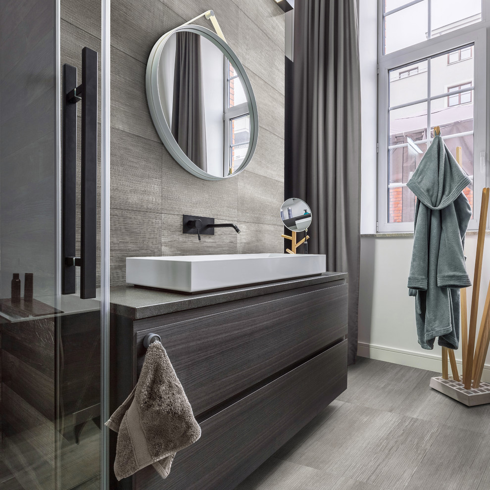 Exemple d'une salle de bain principale tendance de taille moyenne avec un carrelage gris, des carreaux de porcelaine, un mur gris, un sol en carrelage de porcelaine, un sol gris, une cabine de douche à porte battante, un placard à porte plane, des portes de placard grises, une vasque et un plan de toilette gris.