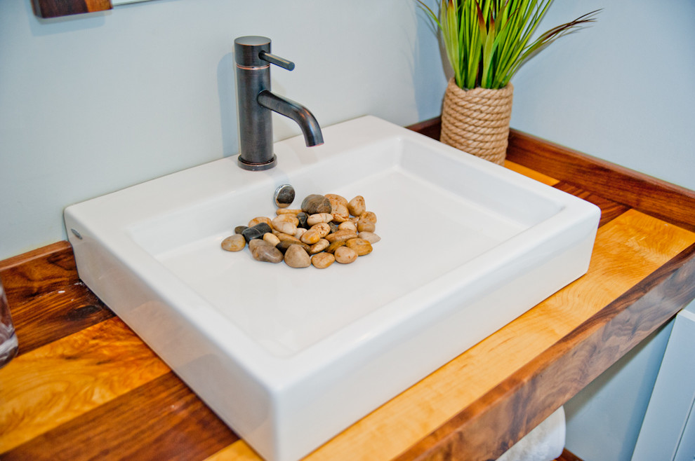 Diseño de cuarto de baño actual pequeño con lavabo sobreencimera, encimera de madera, sanitario de una pieza, paredes grises, suelo de madera en tonos medios y aseo y ducha
