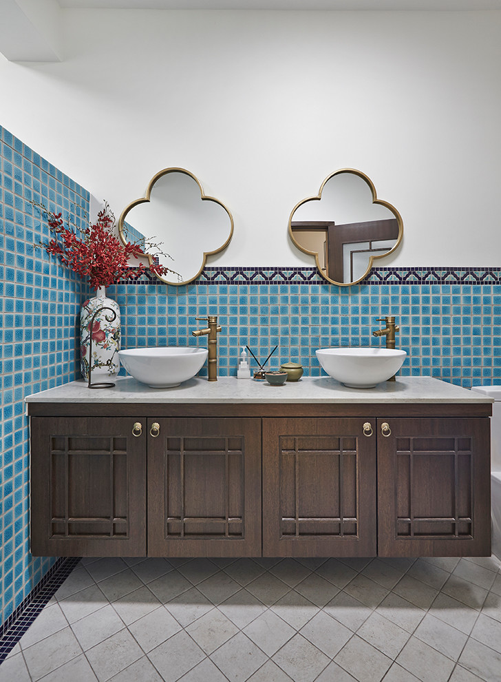 Cette image montre une salle de bain méditerranéenne en bois foncé avec un placard avec porte à panneau encastré, un carrelage bleu, un mur blanc, une vasque, un sol gris et un plan de toilette gris.