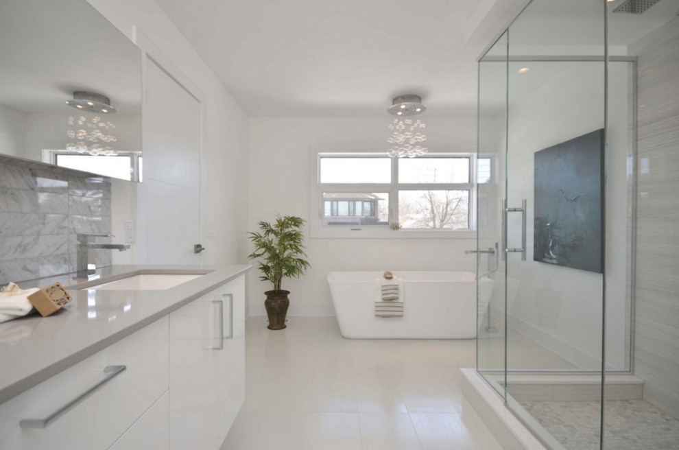 Пример оригинального дизайна: большая главная ванная комната в стиле модернизм с плоскими фасадами, белыми фасадами, отдельно стоящей ванной, угловым душем, врезной раковиной, столешницей из искусственного кварца, раздельным унитазом, белыми стенами и полом из керамогранита