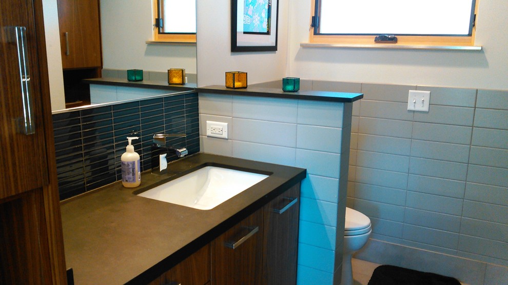 Exemple d'une salle d'eau moderne en bois brun avec un lavabo encastré, un placard à porte plane, un carrelage gris, un carrelage en pâte de verre, un mur gris, un sol en carrelage de porcelaine, un sol gris et un plan de toilette noir.