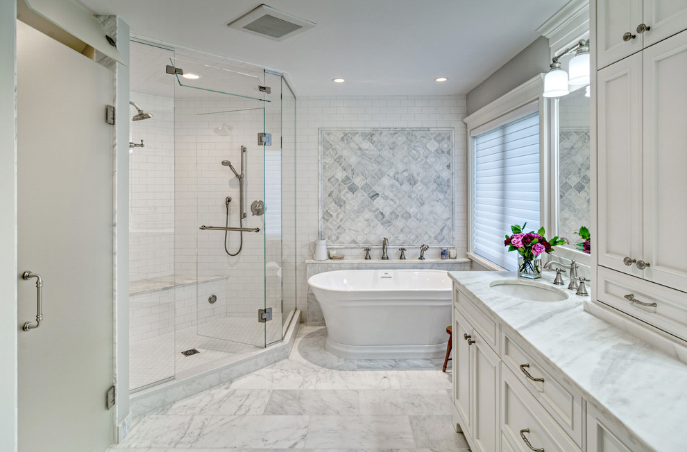 This is an example of a medium sized traditional ensuite bathroom in Minneapolis with freestanding cabinets, white cabinets, a freestanding bath, a double shower, a two-piece toilet, white tiles, porcelain tiles, grey walls, marble flooring, a submerged sink, marble worktops, white floors, a hinged door and white worktops.