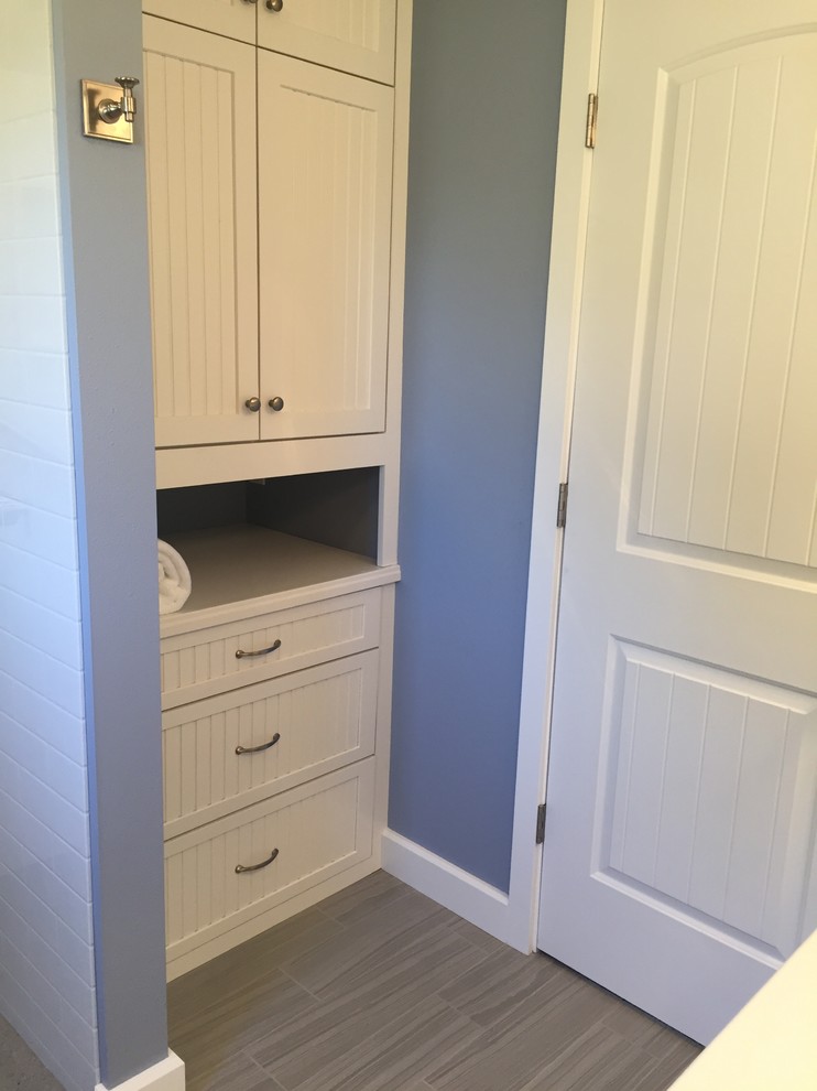 Lantlig inredning av ett litet en-suite badrum, med luckor med profilerade fronter, vita skåp, blå väggar, klinkergolv i porslin, träbänkskiva och grått golv