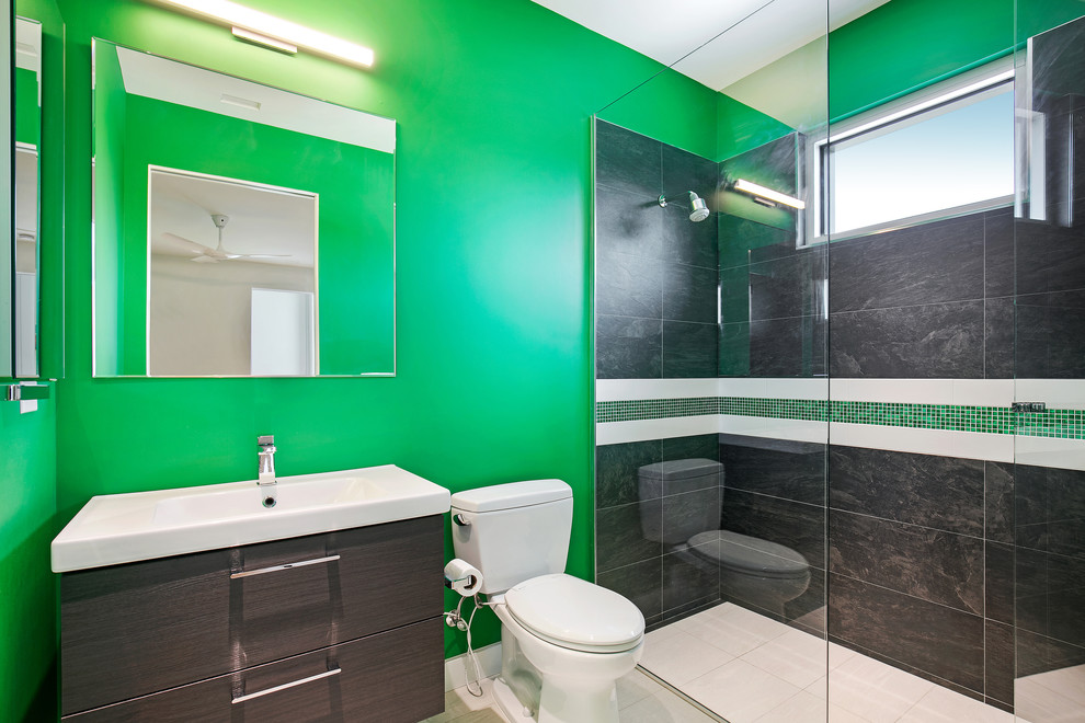 Example of a mid-sized minimalist kids' black and white tile and porcelain tile porcelain tile and white floor walk-in shower design in Tampa with flat-panel cabinets, brown cabinets, a two-piece toilet, green walls, an integrated sink, solid surface countertops, a hinged shower door and white countertops