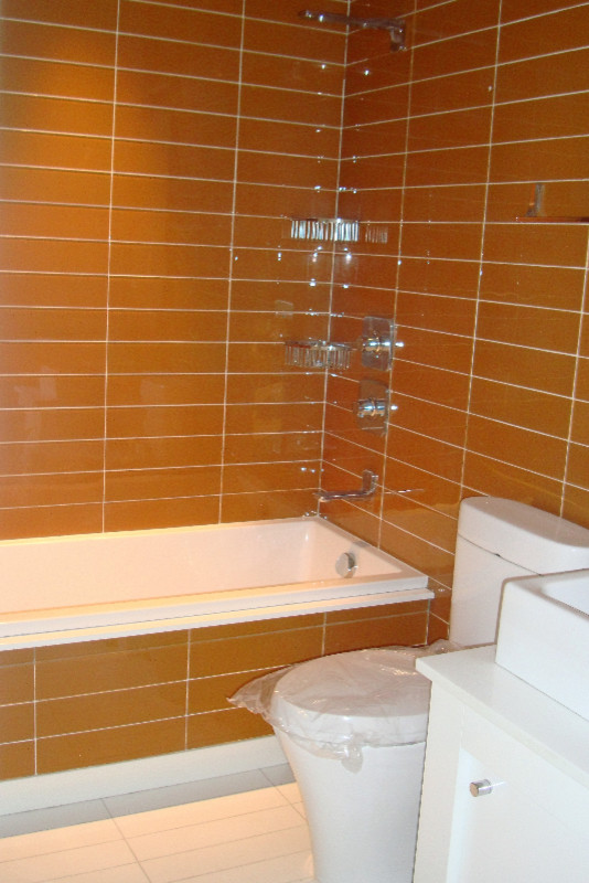 Photo of a medium sized traditional ensuite bathroom in New York with white cabinets, an alcove bath, a shower/bath combination, a two-piece toilet, porcelain tiles, orange walls, porcelain flooring, a vessel sink, solid surface worktops, shaker cabinets and orange tiles.