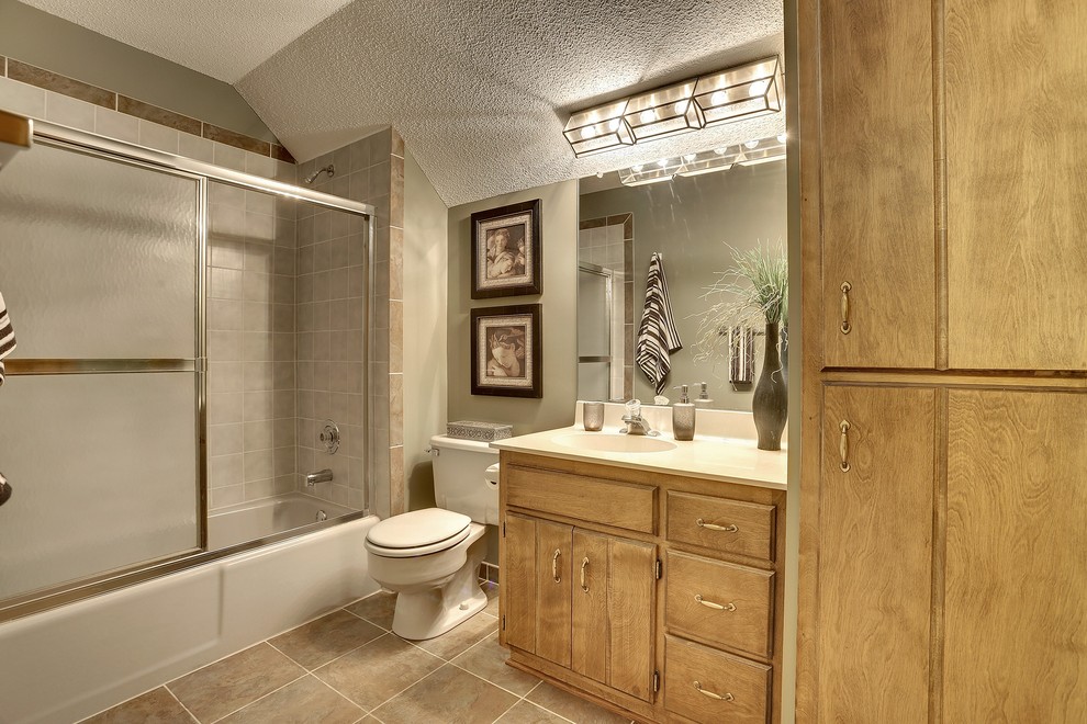 Cette image montre une salle de bain traditionnelle en bois clair avec un lavabo intégré, un placard avec porte à panneau surélevé, un combiné douche/baignoire, WC à poser, un mur vert et un sol en carrelage de porcelaine.