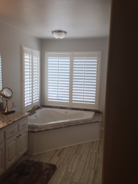 Photo of an expansive classic ensuite bathroom in Other with raised-panel cabinets, white cabinets, a corner bath, white walls, vinyl flooring, a submerged sink and granite worktops.