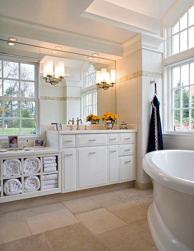 На фото: большая главная ванная комната в классическом стиле с фасадами с выступающей филенкой, белыми фасадами, отдельно стоящей ванной, белой плиткой, керамической плиткой, полом из керамогранита, врезной раковиной и столешницей из искусственного камня