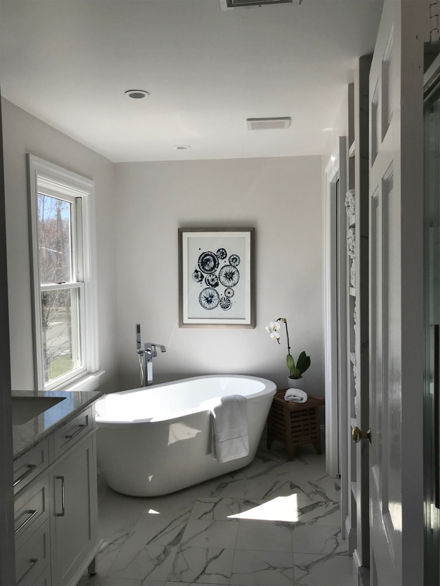 На фото: главная ванная комната в современном стиле с фасадами островного типа, светлыми деревянными фасадами, отдельно стоящей ванной, серыми стенами, полом из травертина, монолитной раковиной, мраморной столешницей, зеленым полом и белой столешницей с
