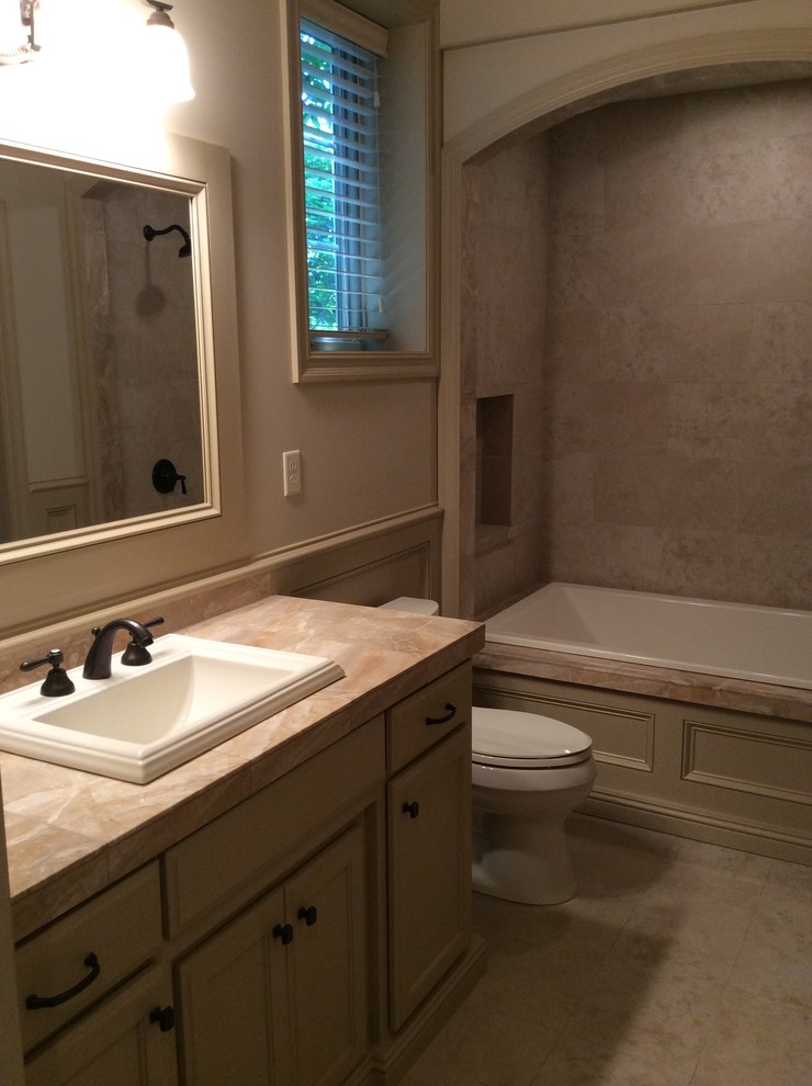 Cette image montre une salle de bain traditionnelle de taille moyenne avec un combiné douche/baignoire, un mur beige, un lavabo posé, un placard avec porte à panneau encastré et des portes de placard beiges.