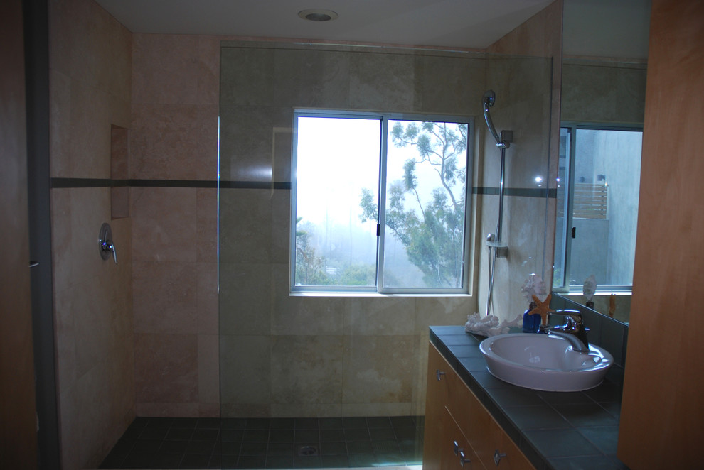 На фото: ванная комната среднего размера в современном стиле с настольной раковиной, плоскими фасадами, светлыми деревянными фасадами, открытым душем, унитазом-моноблоком, зеленой плиткой, полом из травертина и столешницей из плитки