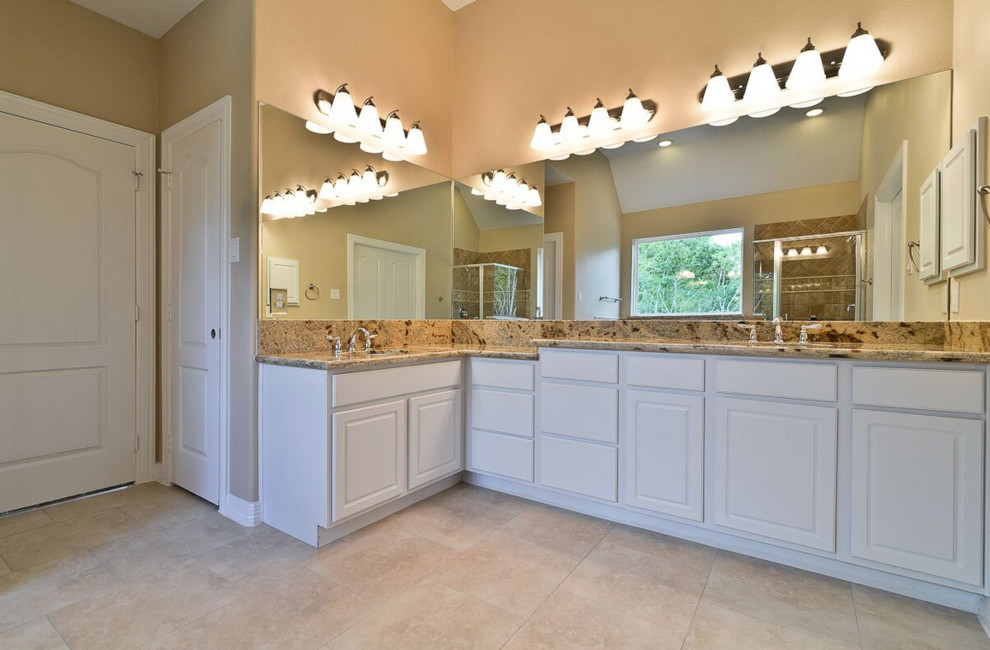 ヒューストンにある中くらいなトランジショナルスタイルのおしゃれなマスターバスルーム (レイズドパネル扉のキャビネット、白いキャビネット、アルコーブ型シャワー、分離型トイレ、ベージュのタイル、茶色いタイル、セラミックタイル、ベージュの壁、トラバーチンの床、アンダーカウンター洗面器、御影石の洗面台、アルコーブ型浴槽) の写真