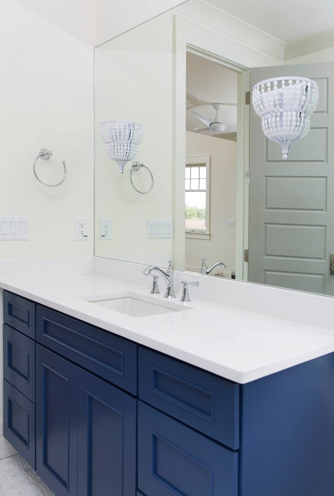 Réalisation d'une salle de bain principale tradition de taille moyenne avec un placard avec porte à panneau encastré, des portes de placard bleues, un mur blanc, un sol en galet, un lavabo encastré, un plan de toilette en surface solide et un sol blanc.