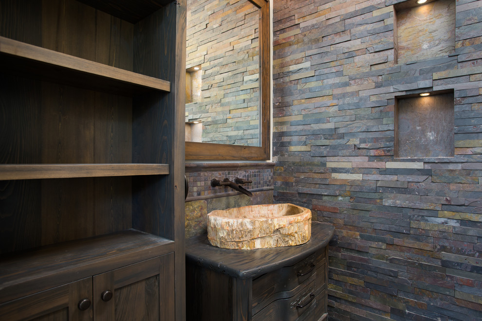 Immagine di una stanza da bagno stile rurale con consolle stile comò, ante in legno bruno, piastrelle in pietra, lavabo a bacinella e top in legno