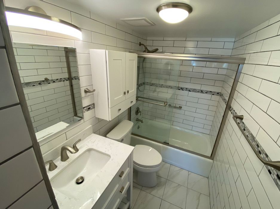 Cette image montre une petite salle d'eau traditionnelle avec un placard en trompe-l'oeil, des portes de placard blanches, une baignoire en alcôve, un combiné douche/baignoire, WC séparés, un carrelage blanc, un carrelage métro, un mur blanc, un sol en carrelage de céramique, un lavabo encastré, un plan de toilette en quartz modifié, un sol blanc, une cabine de douche à porte coulissante, un plan de toilette blanc, meuble simple vasque, meuble-lavabo sur pied et une niche.
