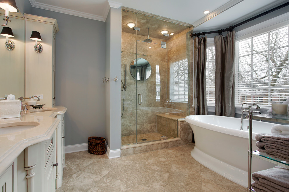 Cette image montre une grande salle de bain principale traditionnelle avec une douche d'angle, WC séparés, un placard à porte shaker, des portes de placard blanches, une baignoire posée, un mur gris, un sol en travertin, un lavabo encastré et un plan de toilette en calcaire.