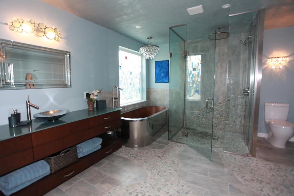 На фото: большая главная ванная комната в стиле модернизм с плоскими фасадами, темными деревянными фасадами, душем без бортиков, раздельным унитазом, синими стенами, полом из галечной плитки, настольной раковиной, стеклянной столешницей, душем с распашными дверями и отдельно стоящей ванной