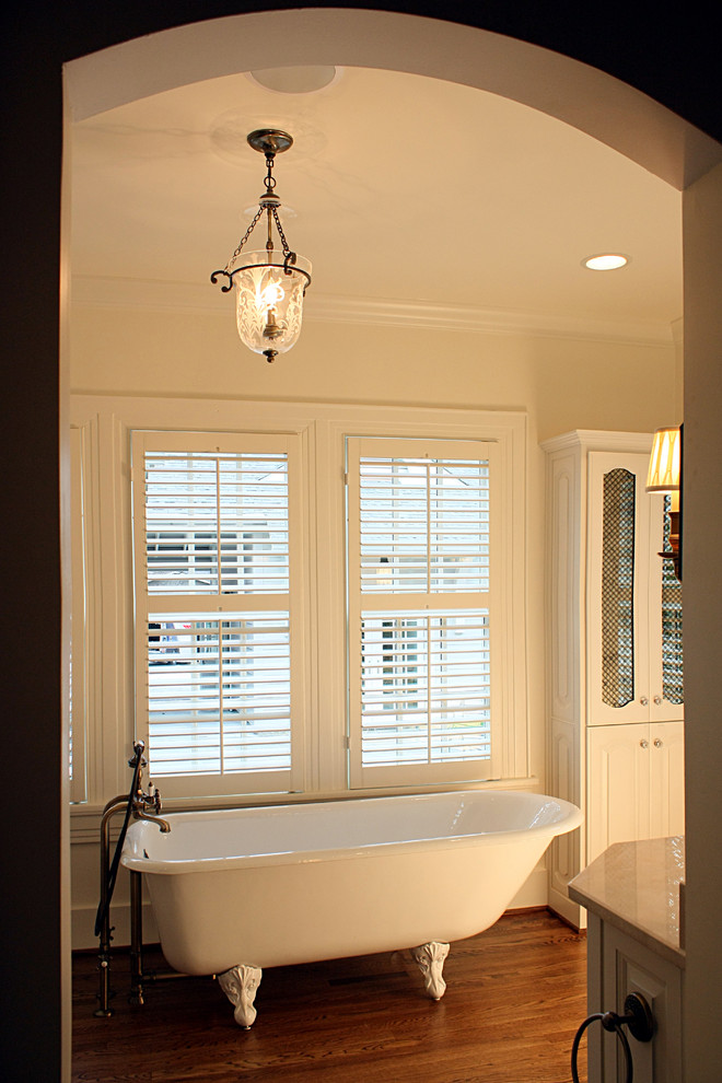 Example of a large classic dark wood floor claw-foot bathtub design in Nashville with glass-front cabinets, white cabinets and beige walls