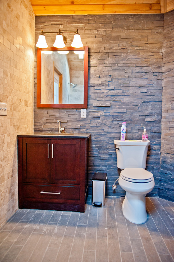Example of a large trendy 3/4 beige tile, gray tile and stone tile slate floor doorless shower design in New York with shaker cabinets, dark wood cabinets, a one-piece toilet, multicolored walls, an undermount sink and solid surface countertops
