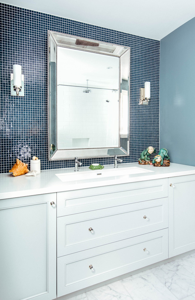 Пример оригинального дизайна: детская ванная комната среднего размера в стиле неоклассика (современная классика) с раковиной с несколькими смесителями, серыми фасадами, синей плиткой, плиткой мозаикой, синими стенами, столешницей из искусственного кварца, душем над ванной, унитазом-моноблоком, мраморным полом, ванной в нише, белым полом, шторкой для ванной, белой столешницей и фасадами с утопленной филенкой
