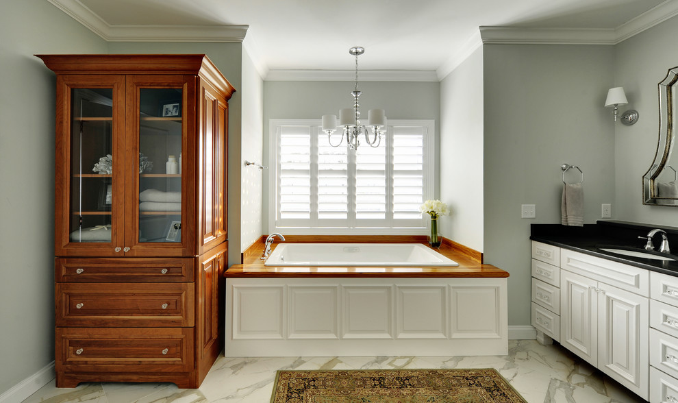 Imagen de cuarto de baño clásico con lavabo bajoencimera, puertas de armario blancas y bañera encastrada