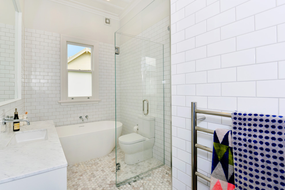 Exemple d'une petite douche en alcôve chic avec des portes de placard blanches, une baignoire indépendante, WC à poser, un carrelage blanc, un carrelage métro, un mur blanc, un sol en carrelage de terre cuite, un plan de toilette en marbre et un lavabo encastré.