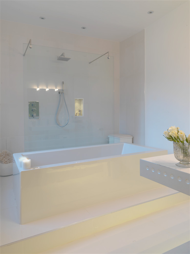 Photo of a large contemporary ensuite bathroom in Oxfordshire with a submerged sink, flat-panel cabinets, white cabinets, solid surface worktops, a freestanding bath, a built-in shower, a wall mounted toilet, white tiles, ceramic tiles, white walls and ceramic flooring.