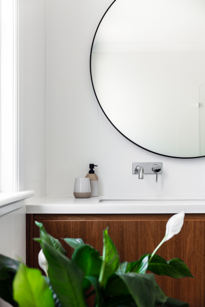 Idée de décoration pour une salle de bain minimaliste en bois brun de taille moyenne avec un carrelage blanc, des carreaux de céramique, un mur blanc, un lavabo encastré, un plan de toilette en quartz modifié et un plan de toilette blanc.