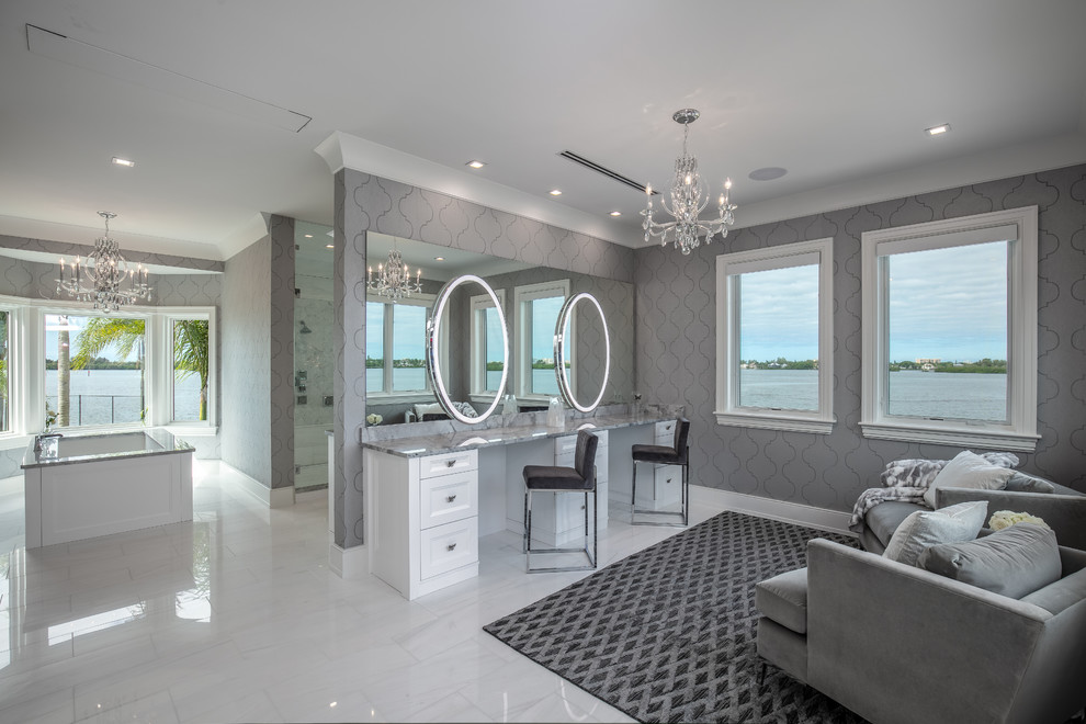タンパにあるビーチスタイルのおしゃれな浴室 (落し込みパネル扉のキャビネット、白いキャビネット、アンダーマウント型浴槽、グレーの壁、大理石の床、白い床、グレーの洗面カウンター) の写真