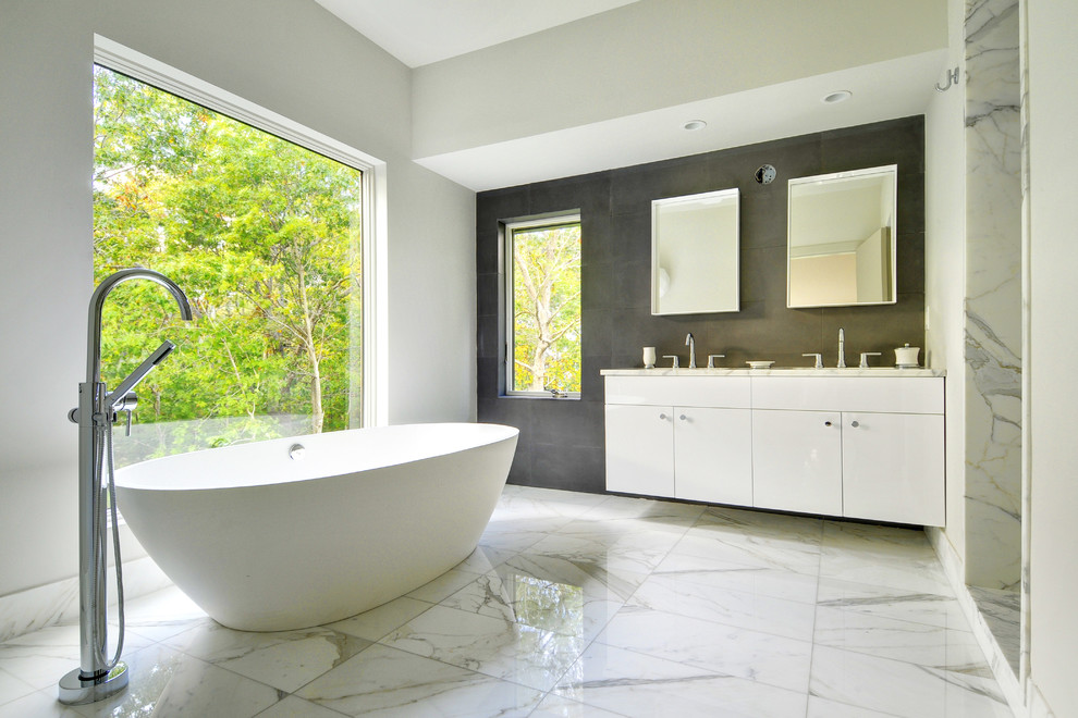 Photo of a large contemporary ensuite bathroom in Boston with marble worktops, flat-panel cabinets, white cabinets, a freestanding bath, a walk-in shower, white tiles, stone tiles, white walls, marble flooring, an open shower, a submerged sink and grey floors.
