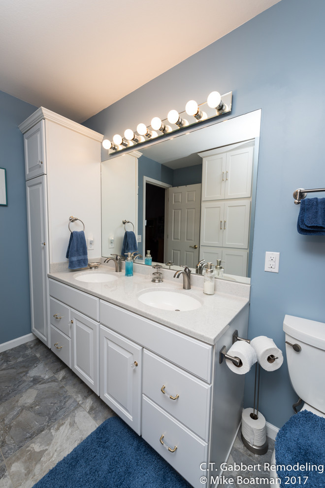 Immagine di una stanza da bagno con doccia minimal di medie dimensioni con ante con bugna sagomata, ante bianche, pareti blu, pavimento in laminato, lavabo integrato, top in onice, pavimento grigio e doccia con tenda