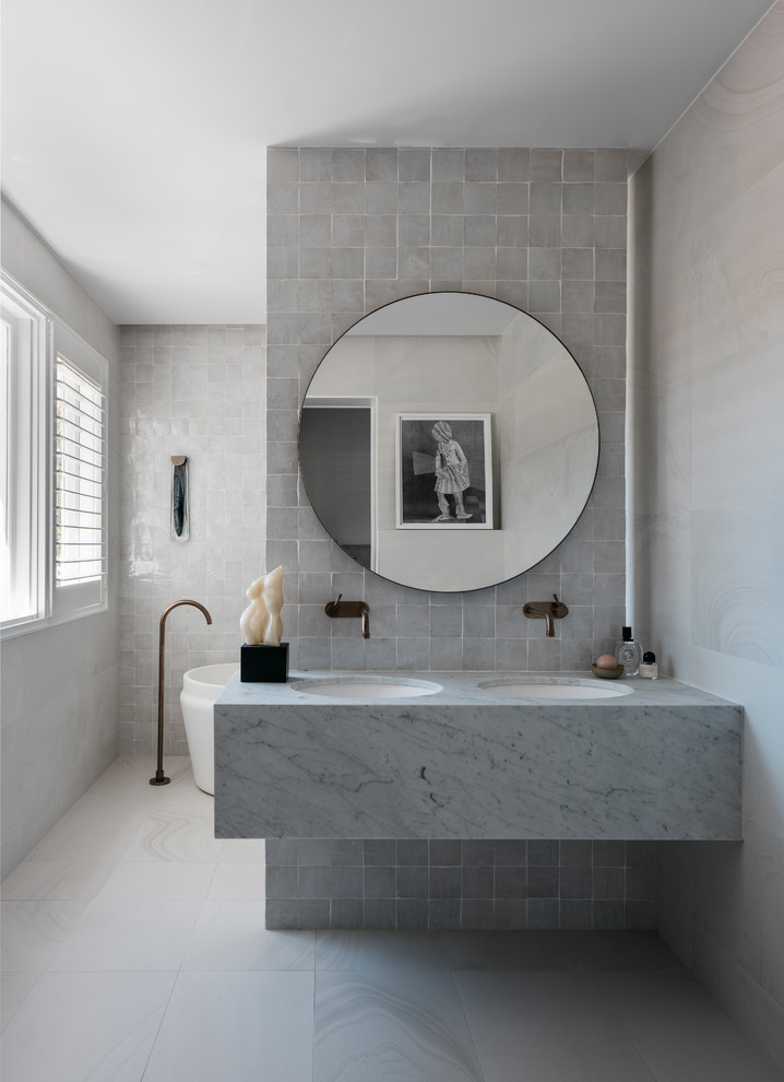 Exemple d'une grande salle de bain principale tendance avec une baignoire indépendante, un carrelage blanc, un carrelage de pierre, un mur blanc, un sol en carrelage de céramique, un lavabo encastré, un plan de toilette en granite, un sol blanc et un plan de toilette blanc.